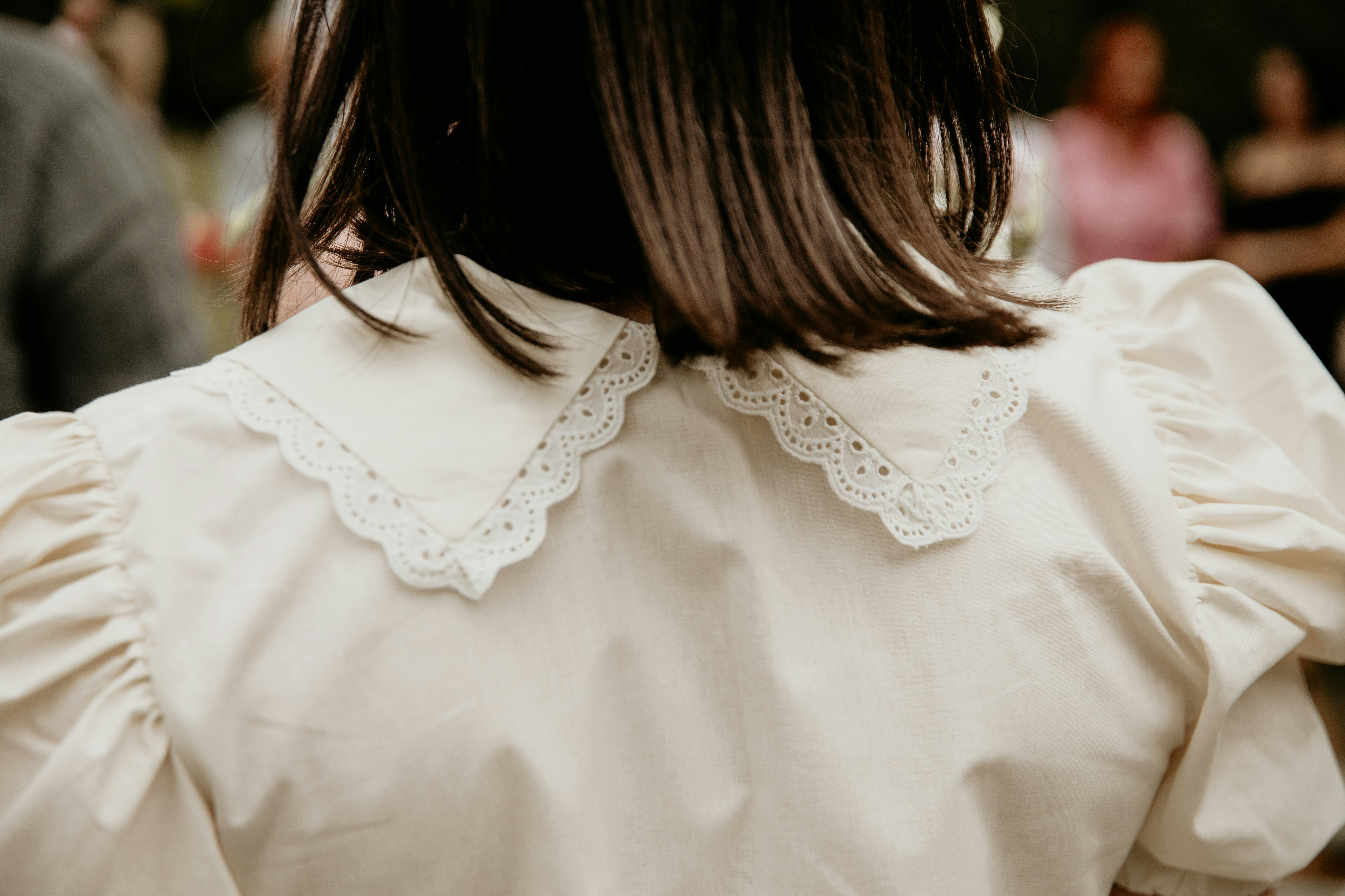 A person wearing a white romantic puff-sleeve blouse with a scalloped eyelet-trimmed collar.
