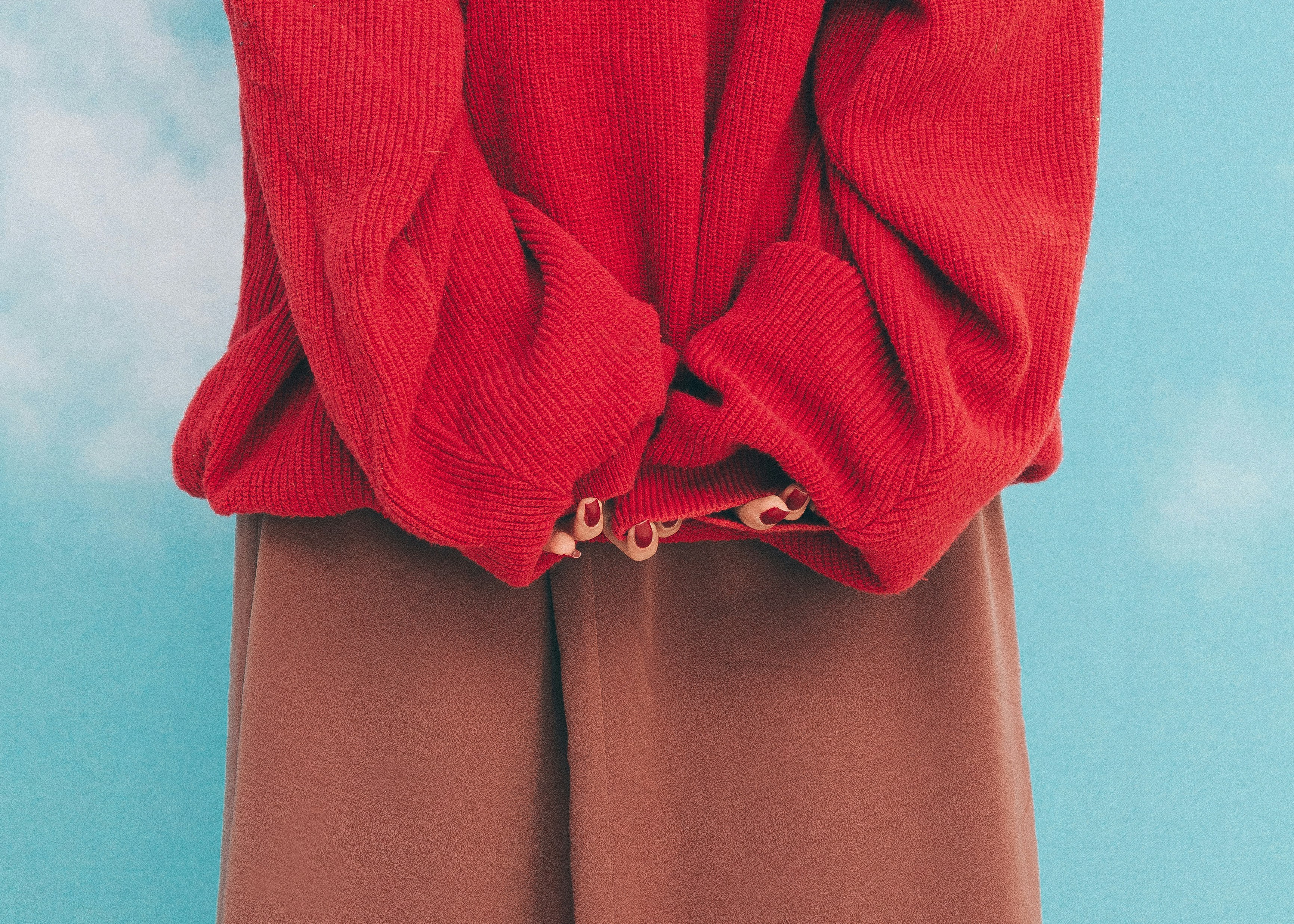Woman wearing a red sweater and brown pants.